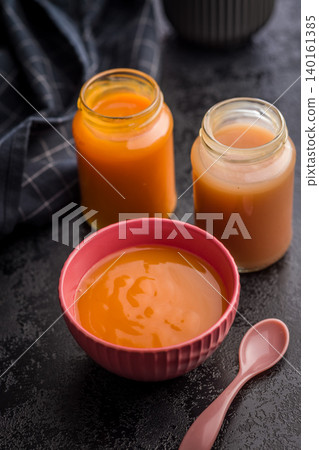 Creamy Pumpkin Soup in Pink Bowl with Glass Jars and Spoon on Dark Surface Creamy Pumpkin Soup in Pink Bowl with Glass Jars and Spoon on Dark Surface 140161385