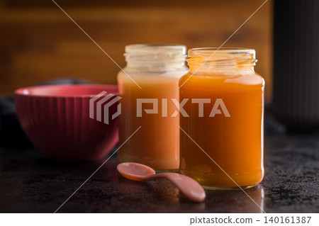Homemade Baby Food Carrot Puree in Glass Jars with Bowl and Spoon on Dark Surface Homemade Baby Food Carrot Puree in Glass Jars with Bowl and Spoon on Dark Surface 140161387