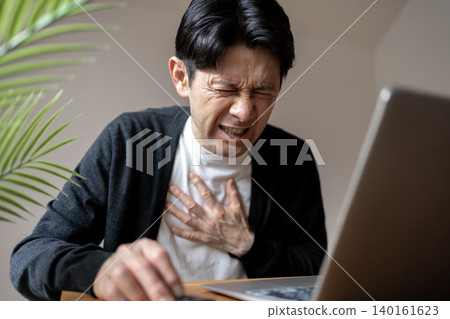 A middle-aged man clutches his chest after being suddenly struck by chest pain while working at his desk. 140161623