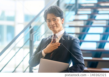 A businessman with his hand on his chest, holding a laptop. 140162321