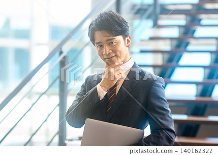A businessman with his hand on his chin, thinking about his laptop. A businessman with his hand on his chin, thinking about his laptop. 140162322