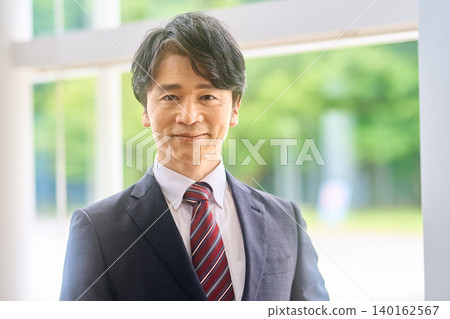 A portrait of a businessman smiling by a bright window. 140162567