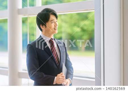 A businessman looking out the window with his laptop in his hand. 140162569
