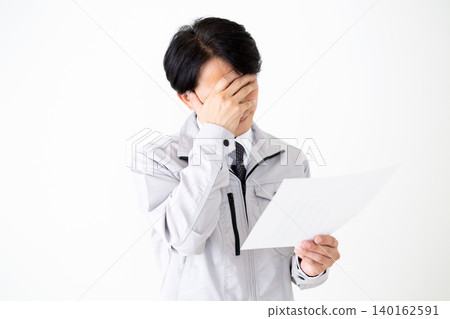 一位身穿灰色工作服的中年商人,在白色背景下看著文件,神情沮喪。 一位身穿灰色工作服的中年商人,在白色背景下看著文件,神情沮喪。 140162591