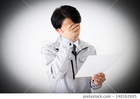 一位身穿灰色工作服的中年商人,在白色背景下看著文件,神情沮喪。 一位身穿灰色工作服的中年商人,在白色背景下看著文件,神情沮喪。 140162605