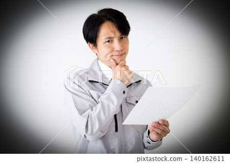 A middle-aged businessman in gray work clothes, looking at documents and pondering, against a white background. A middle-aged businessman in gray work clothes, looking at documents and pondering, against a white background. 140162611