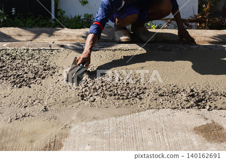 Construction worker's hand using a trowel to smooth fresh gravel mixed cement on a road surface. Construction worker's hand using a trowel to smooth fresh gravel mixed cement on a road surface. 140162691