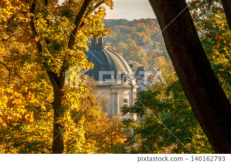 A majestic dome structure peeks through a canopy of golden and green leaves during a picturesque autumn day in a European city park A majestic dome structure peeks through a canopy of golden and green leaves during a picturesque autumn day in a European city park 140162793