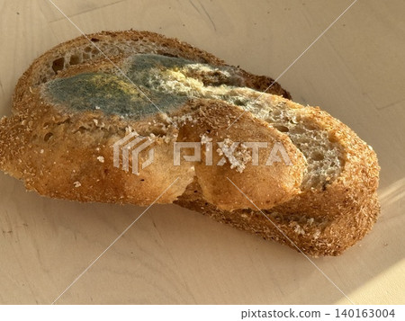 Moldy slice of whole grain bread with blue and green mold on wooden surface 140163004