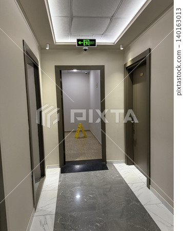 Hallway with wet floor sign, open doors, marble floor, and emergency exit sign, suitable for backgrounds Hallway with wet floor sign, open doors, marble floor, and emergency exit sign, suitable for backgrounds 140163013