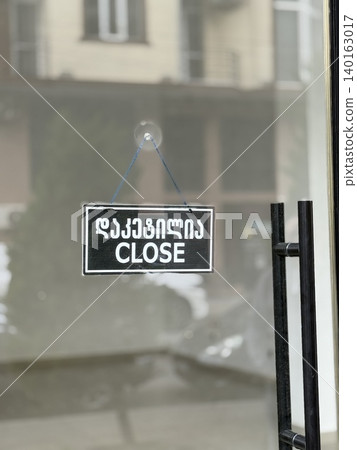 Close sign hanging on glass door of storefront, reflecting urban street background Close sign hanging on glass door of storefront, reflecting urban street background 140163017