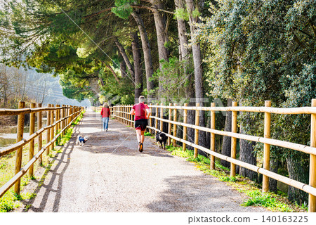 People walking and jogging along the path by the reservoir in the Sant Llorenc de Montgai Nature Reserve, Noguera region, Lleida, Catalonia People walking and jogging along the path by the reservoir in the Sant Llorenc de Montgai Nature Reserve, Noguera region, Lleida, Catalonia 140163225