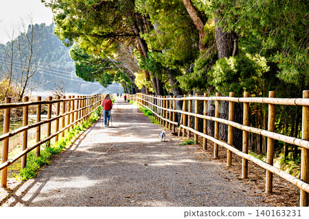 Woman walking her dog along the path by the reservoir in the Sant Llorenc de Montgai Nature Reserve, Noguera region, Lleida, Catalonia Woman walking her dog along the path by the reservoir in the Sant Llorenc de Montgai Nature Reserve, Noguera region, Lleida, Catalonia 140163231
