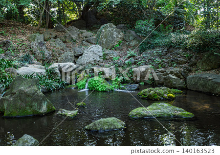 A small waterfall in Rikugien Garden, gently flowing over moss-covered rock faces, with beautiful rock formations on the water's surface. November 2023. A small waterfall in Rikugien Garden, gently flowing over moss-covered rock faces, with beautiful rock formations on the water's surface. November 2023. 140163523