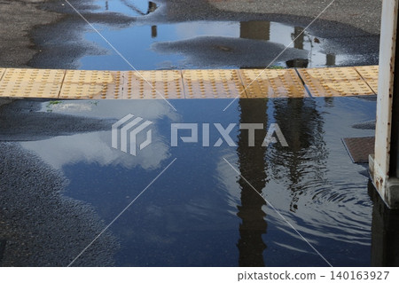 A landscape with a puddle reflecting the blue sky and clouds. A landscape with a puddle reflecting the blue sky and clouds. 140163927