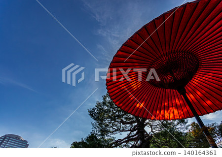 A traditional red outdoor tea ceremony umbrella and its beautifully spreading bamboo frame stand out against the blue sky. November 2023. 140164361