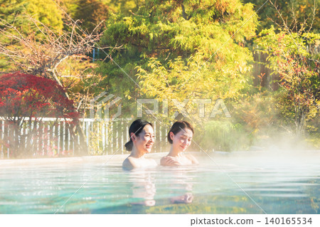 Two women relaxing in an open-air bath with autumn leaves in the background. Two women relaxing in an open-air bath with autumn leaves in the background. 140165534
