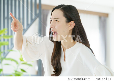 一位年輕的日本女子在客廳裡憤怒地指著別人。 一位年輕的日本女子在客廳裡憤怒地指著別人。 140166144