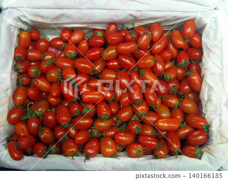 Top-down view of a white paper-lined crate filled with fresh, vibrant red cherry tomatoes. The ripe, oblong tomatoes still have their green stems attached, creating a colorful and textured harvest sce Top-down view of a white paper-lined crate filled with fresh, vibrant red cherry tomatoes. The ripe, oblong tomatoes still have their green stems attached, creating a colorful and textured harvest sce 140166185