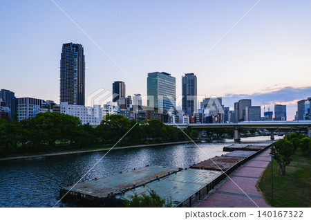 美麗的夜景開始了,黃昏時分,漂浮在堂島川上的駁船和中之島的摩天大樓群構成了一幅美麗的畫面。 美麗的夜景開始了,黃昏時分,漂浮在堂島川上的駁船和中之島的摩天大樓群構成了一幅美麗的畫面。 140167322