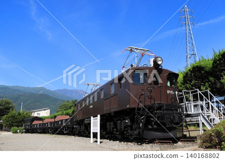 A freight train formation (preserved vehicle) pulled by locomotive EF15-198 stands quietly, watched over by the mountains of the Southern Alps. 140168802