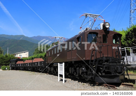 A freight train formation (preserved vehicle) pulled by locomotive EF15-198 stands quietly, watched over by the mountains of the Southern Alps. 140168806