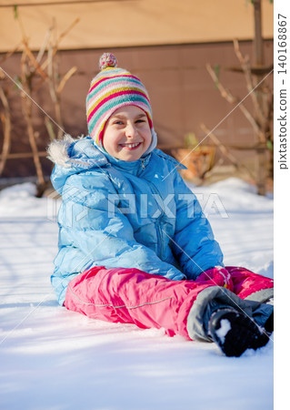 Smiling child colorful winter clothes standing on snow with trees and houses in sunny background Smiling child colorful winter clothes standing on snow with trees and houses in sunny background 140168867