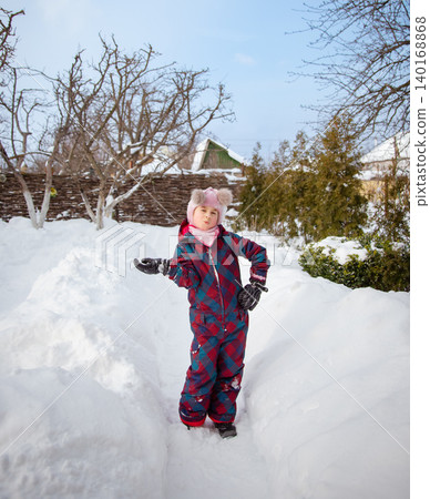 Smiling girl winter clothes holding large snowball standing in deep snow near house wooden fence 140168868