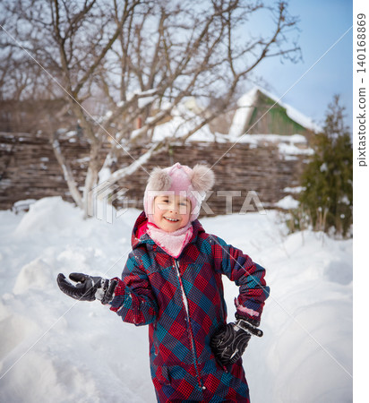 Smiling girl winter clothes holding large snowball standing in deep snow near house wooden fence 140168869