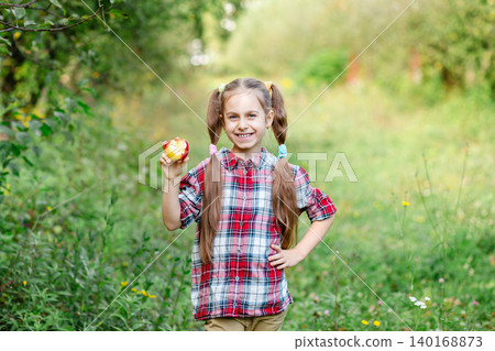 Happy girl holding red apple in orchard smiling at camera during sunny autumn day in countryside Happy girl holding red apple in orchard smiling at camera during sunny autumn day in countryside 140168873