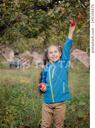 Cheerful girl picking red apple from tree branch while holding another fruit orchard autumn harvest 140168876
