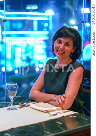 Elegant Woman Enjoying Dinner in a Restaurant with Stunning Night City View Through the Window, Capturing the Essence of Urban Sophistication 140169149