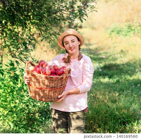 Portrait of woman in hat offering fresh red apples in orchard  140169560