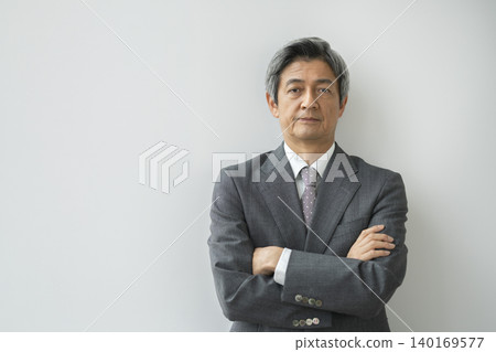 一位六十多歲的男子身穿西裝,雙臂交叉,直視鏡頭。 一位六十多歲的男子身穿西裝,雙臂交叉,直視鏡頭。 140169577