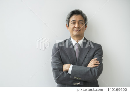 A man in his 60s, wearing a suit and with his arms crossed, smiles and looks directly at the camera. A man in his 60s, wearing a suit and with his arms crossed, smiles and looks directly at the camera. 140169600