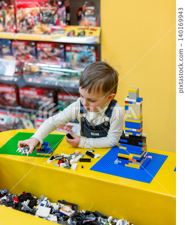 Little boy focused on assembling colorful building bricks bright table inside toy store environment 140169943