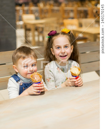 Generated imageTwo children sharing ice cream cone while sitting at wooden table Generated imageTwo children sharing ice cream cone while sitting at wooden table 140170145