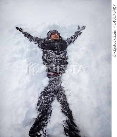 Adult man lying on fresh snow making snow angel with outstretched Adult man lying on fresh snow making snow angel with outstretched 140170407