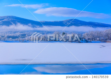 A vast background image of Lake Yamanaka in the early morning during winter, with its pristine white frozen surface and clear blue sky. 140170539