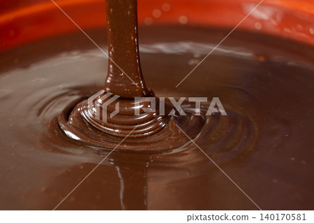 Close-up of rich liquid dark chocolate flowing in a smooth stream Close-up of rich liquid dark chocolate flowing in a smooth stream 140170581