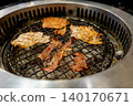 Close up of marinated pork and beef slices grilling on a wire mesh over hot charcoal in a round tabletop stove. Traditional Korean BBQ or Japanese Yakiniku restaurant dining experience. 140170671