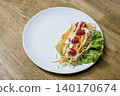 Fresh vegetable salad with shredded carrots, lettuce, and cherry tomatoes drizzled with white cream dressing on a round white plate. Served on a wooden surface. Healthy diet food concept. 140170674