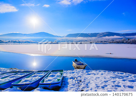 冬日清晨的山中湖:一艘小船漂浮在蔚藍的湖面上,與冉冉升起的太陽形成美麗的對比。 冬日清晨的山中湖:一艘小船漂浮在蔚藍的湖面上,與冉冉升起的太陽形成美麗的對比。 140170675