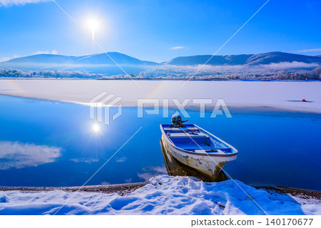 Morning light on Lake Yamanaka in winter: A beautiful contrast between a single boat floating on the blue lake surface and the rising sun. Morning light on Lake Yamanaka in winter: A beautiful contrast between a single boat floating on the blue lake surface and the rising sun. 140170677