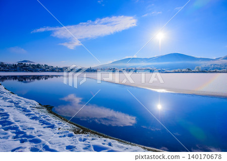 Morning light on Lake Yamanaka in winter: A beautiful contrast between a single boat floating on the blue lake surface and the rising sun. Morning light on Lake Yamanaka in winter: A beautiful contrast between a single boat floating on the blue lake surface and the rising sun. 140170678