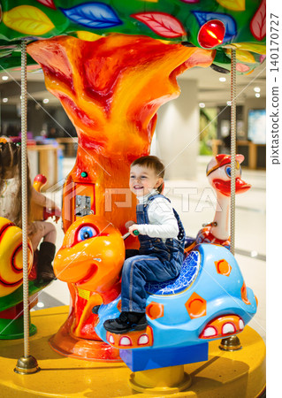 Little boy riding colorful carousel turtle shopping mall amusement area bright decorations Little boy riding colorful carousel turtle shopping mall amusement area bright decorations 140170727