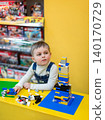 Little boy focused on assembling colorful building bricks at bright yellow table  140170729