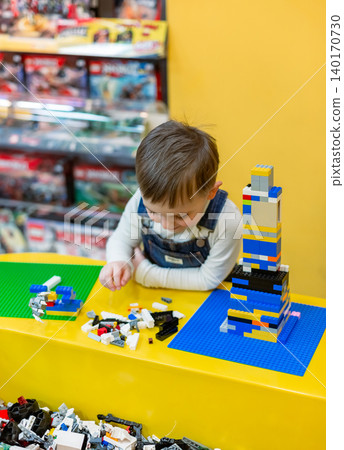Little boy focused on assembling colorful building bricks at bright yellow table  140170730