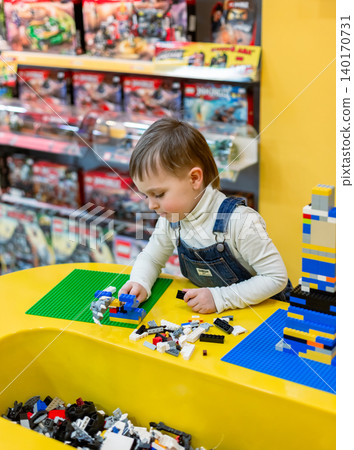Little boy focused on assembling colorful building bricks bright table inside toy store environment 140170731