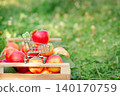 Red apple placed in miniature shopping cart on wooden crate filled with fresh apples in orchard. 140170759